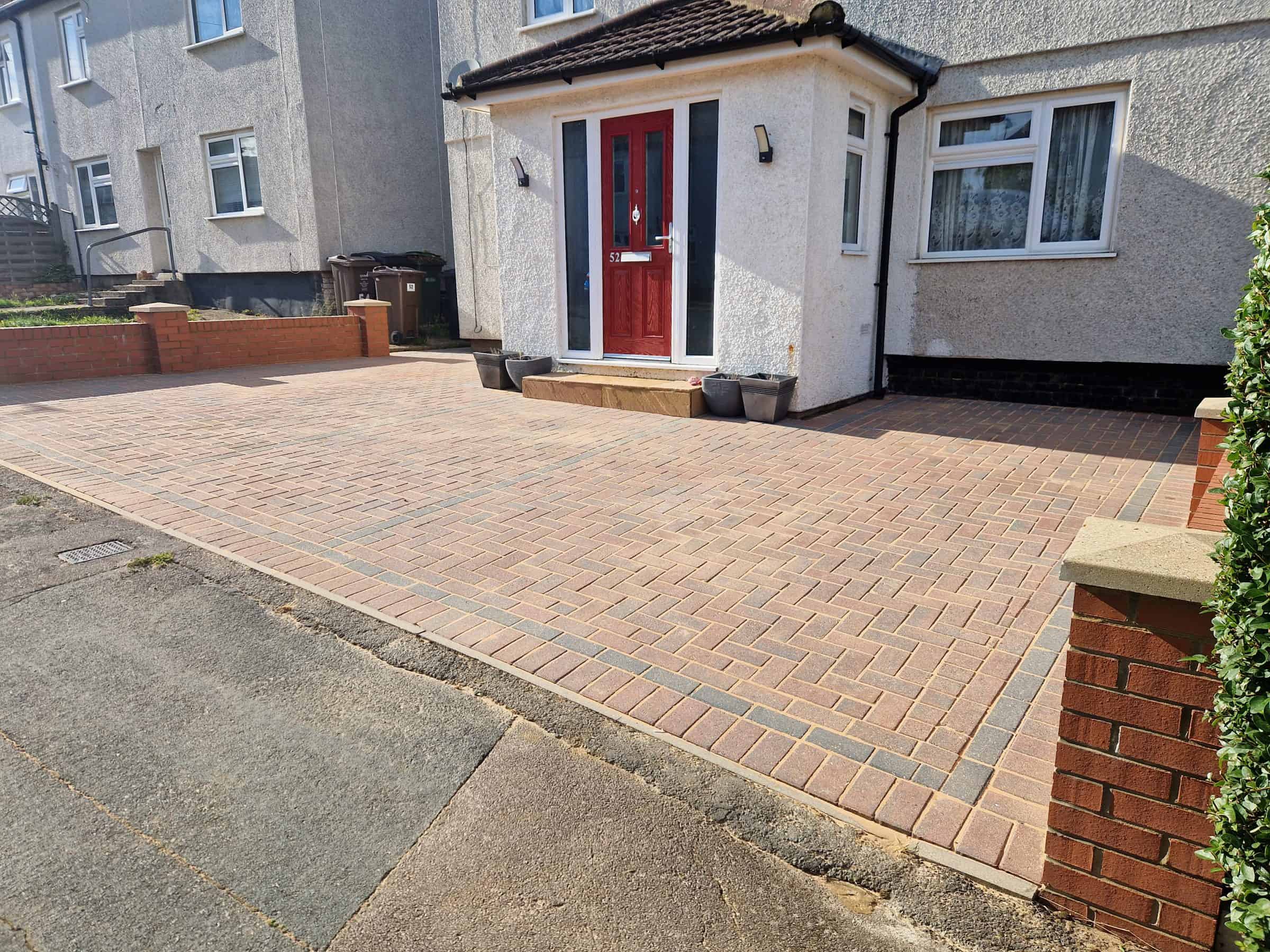 Finished block-paved driveway after cleaning in front of a white semi-detached house with a red front door