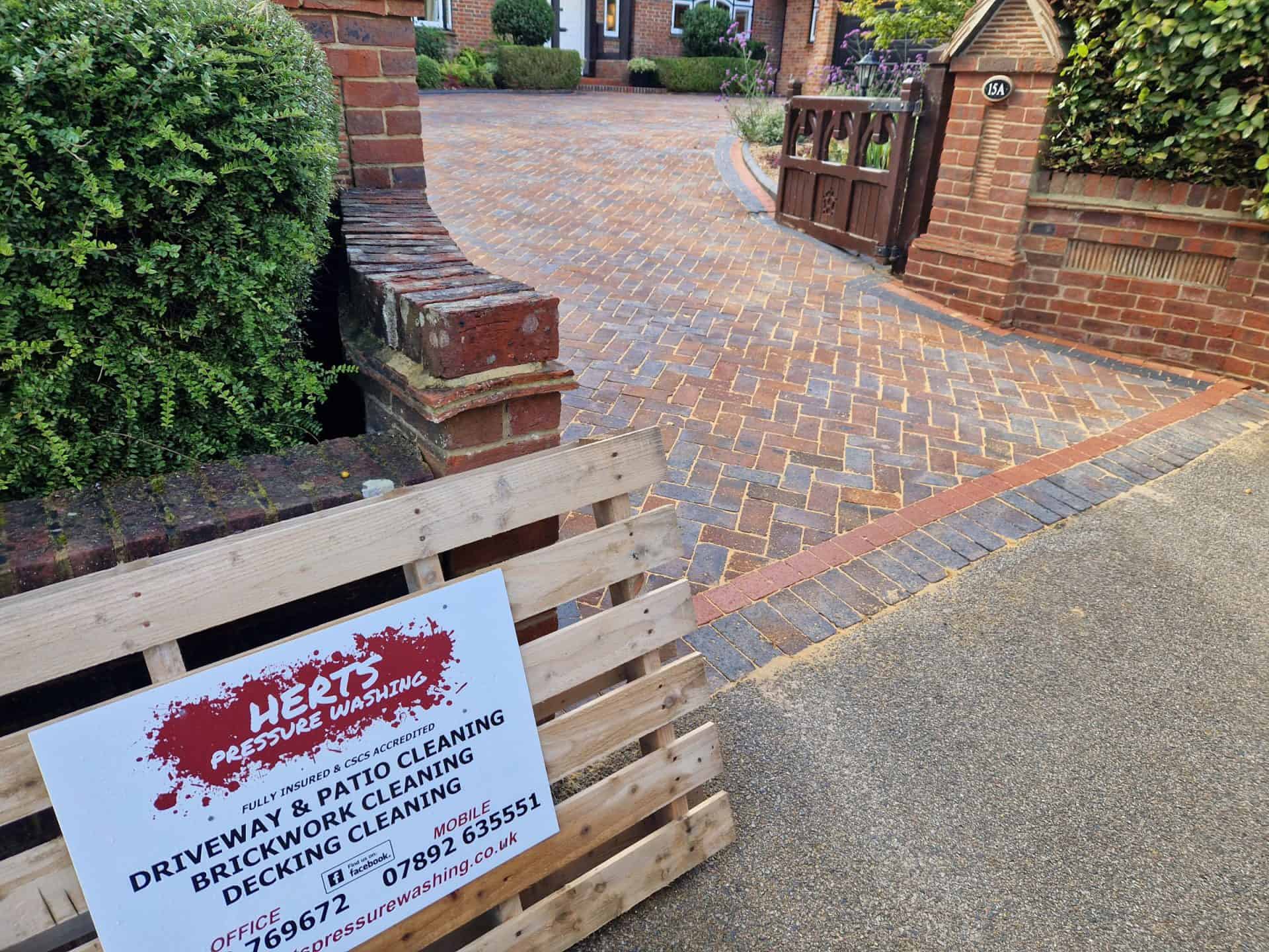 Block paved driveway being pressure washed, with the Herts Pressure Washing sign on the drive