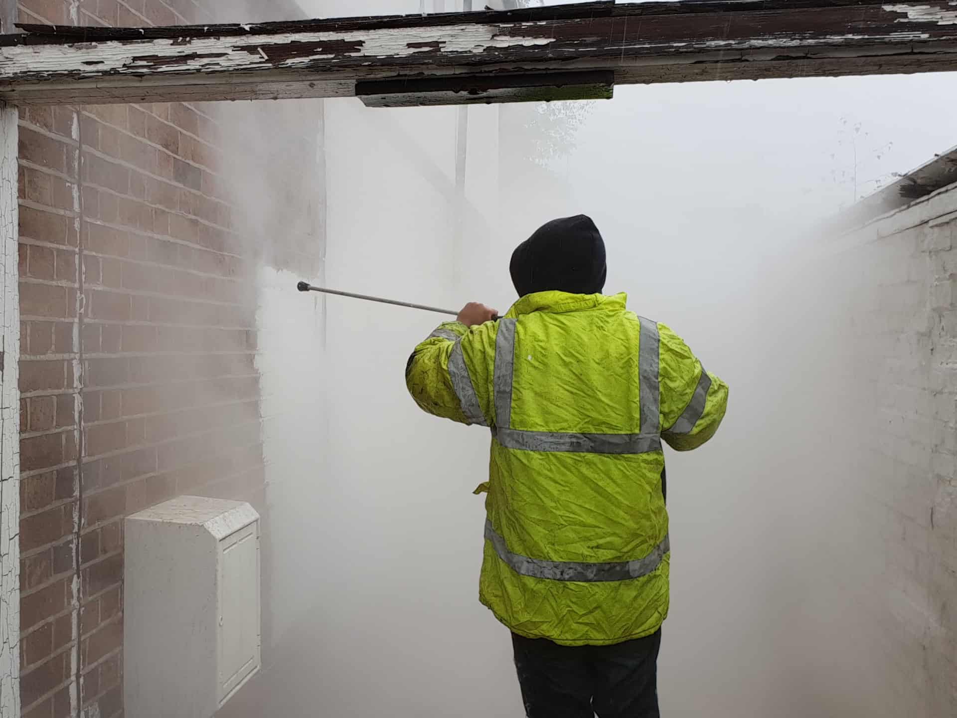 Person in hi-vis jacket pressure washing a brick wall