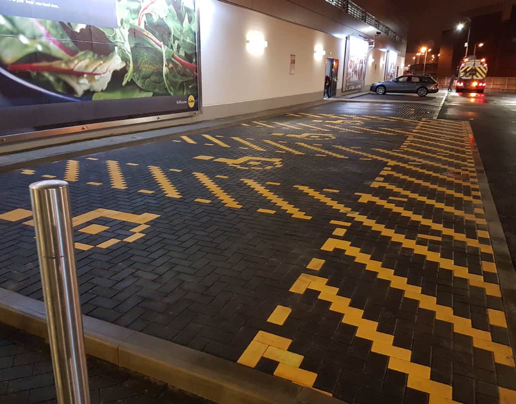 Block paving outside a supermarket pressure washed at night, with the yellow markings bright and clean again