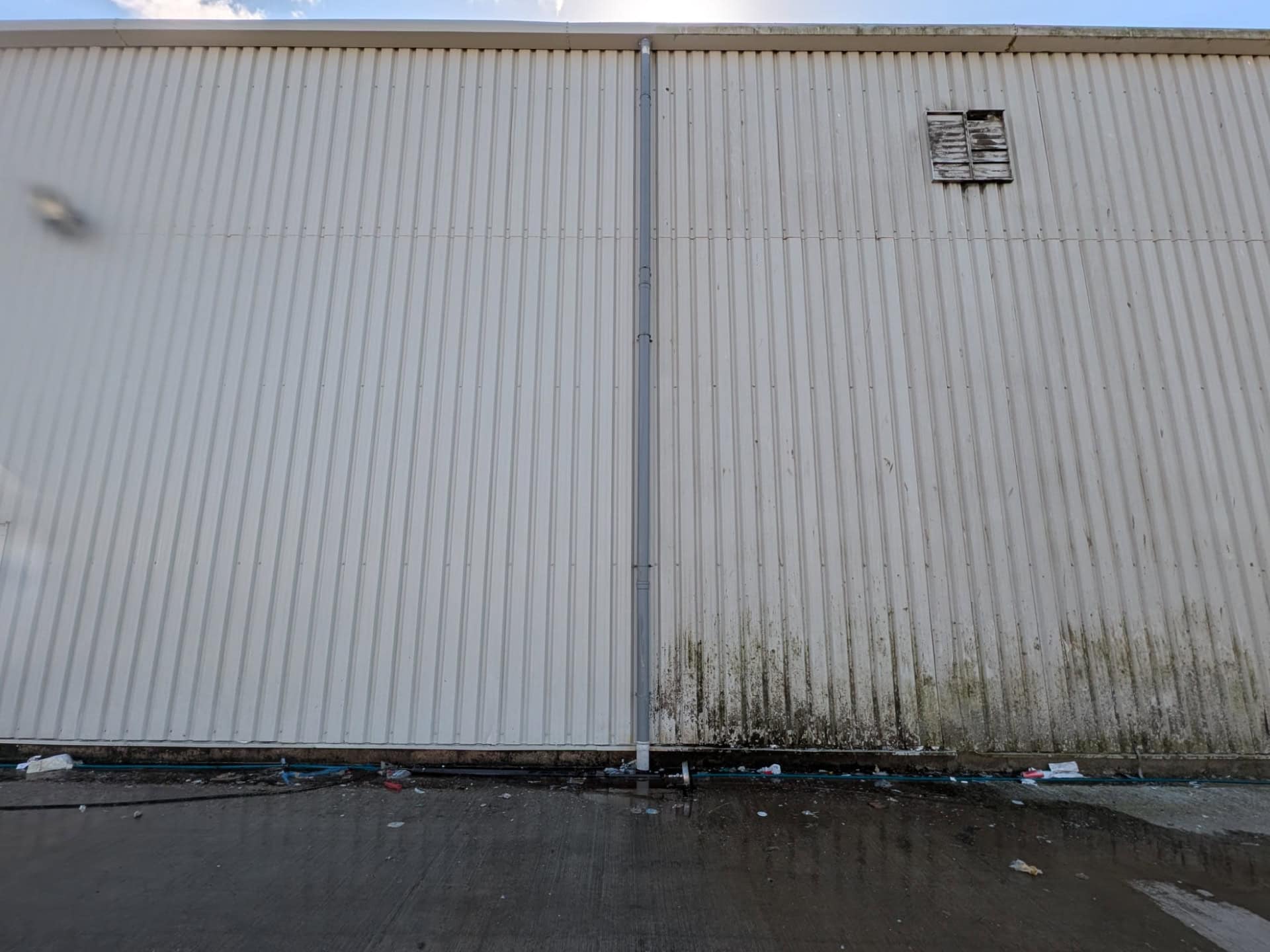 Warehouse cladding part way through cleaning, with the cleaned panels on the left and green algae still on the right