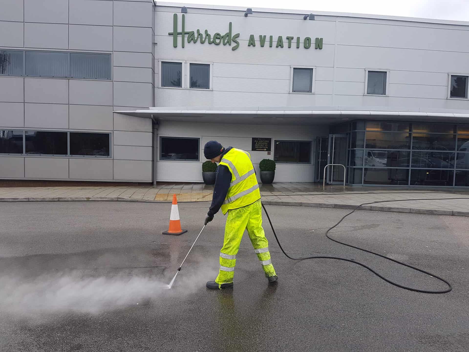 Operator in hi-vis PPE pressure washing outside the Harrods Aviation hangar at Luton Airport
