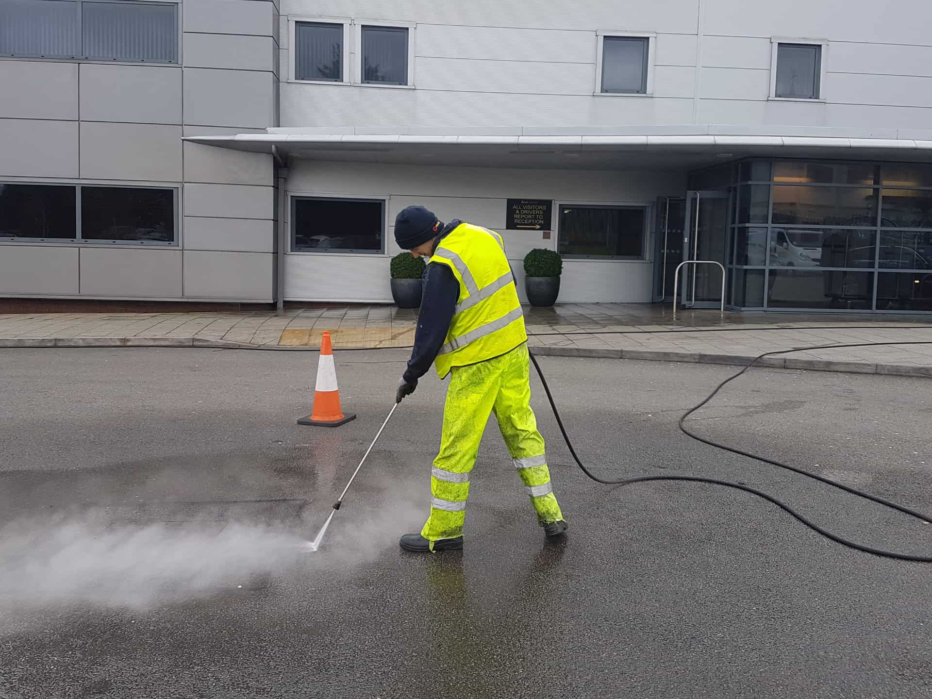 Herts Pressure Washing operative in hi-vis pressure washing tarmac outside a commercial building entrance