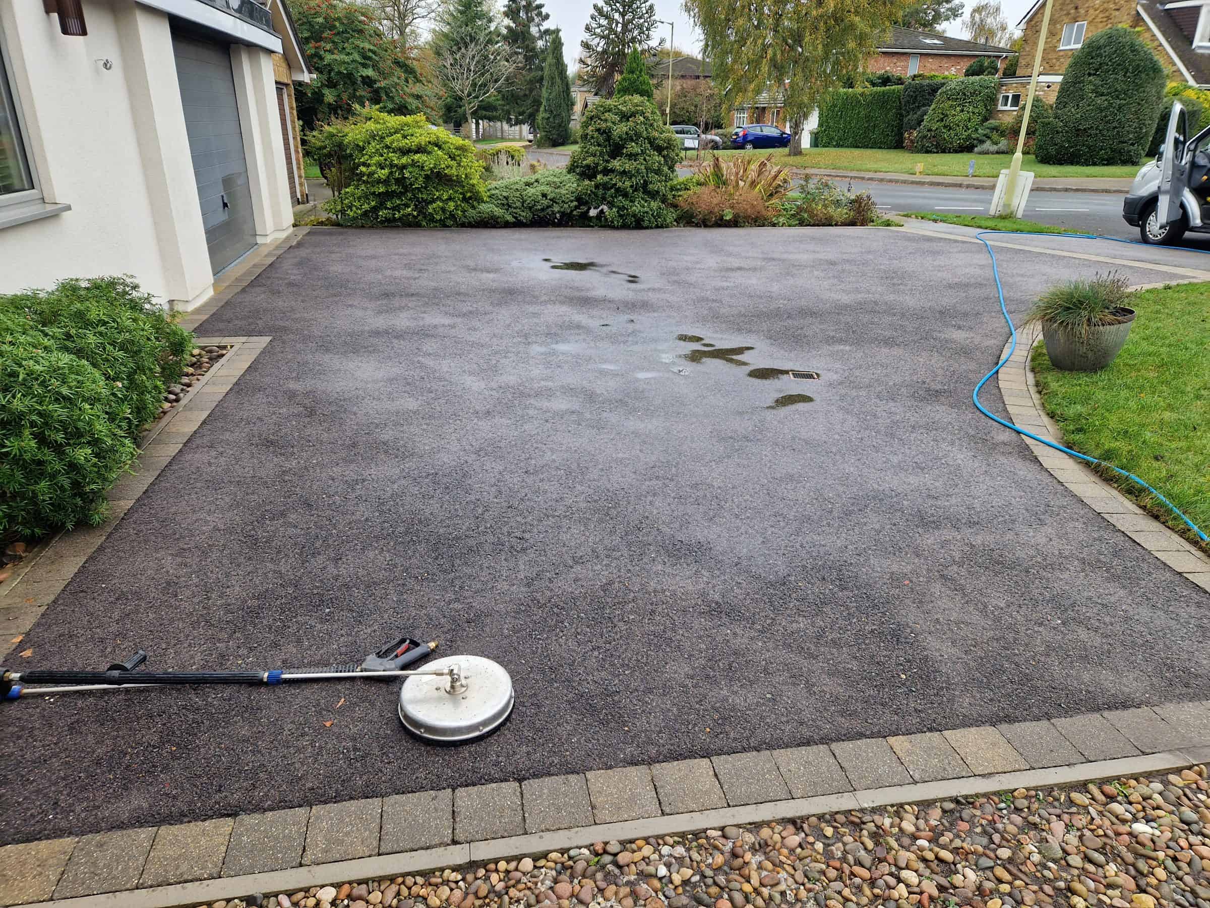 Rotary surface cleaner mid-pass on a tarmac driveway in Hertfordshire, cleaned strip showing against the dirty surface