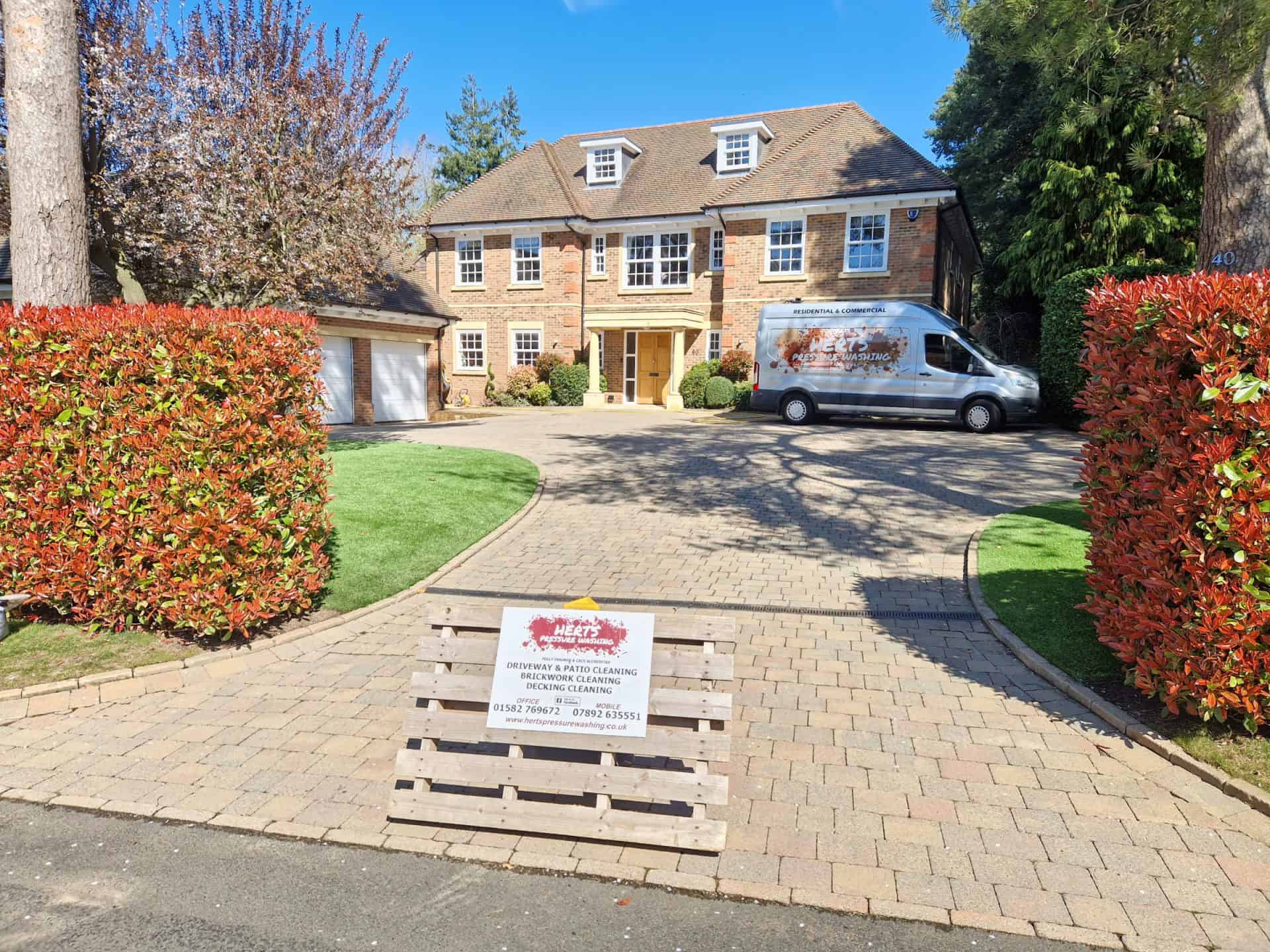 The Herts Pressure Washing van and sign outside a large detached house during a driveway clean