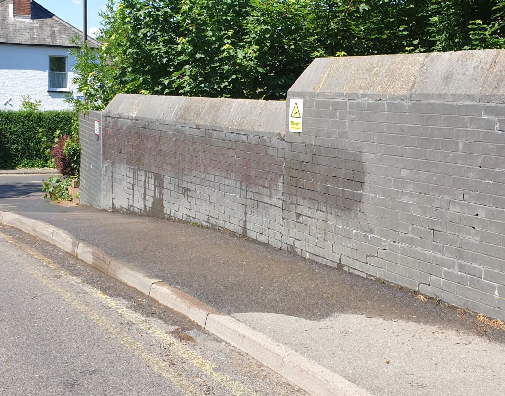 Painted brick bridge wall beside a pavement during graffiti removal in Hertfordshire