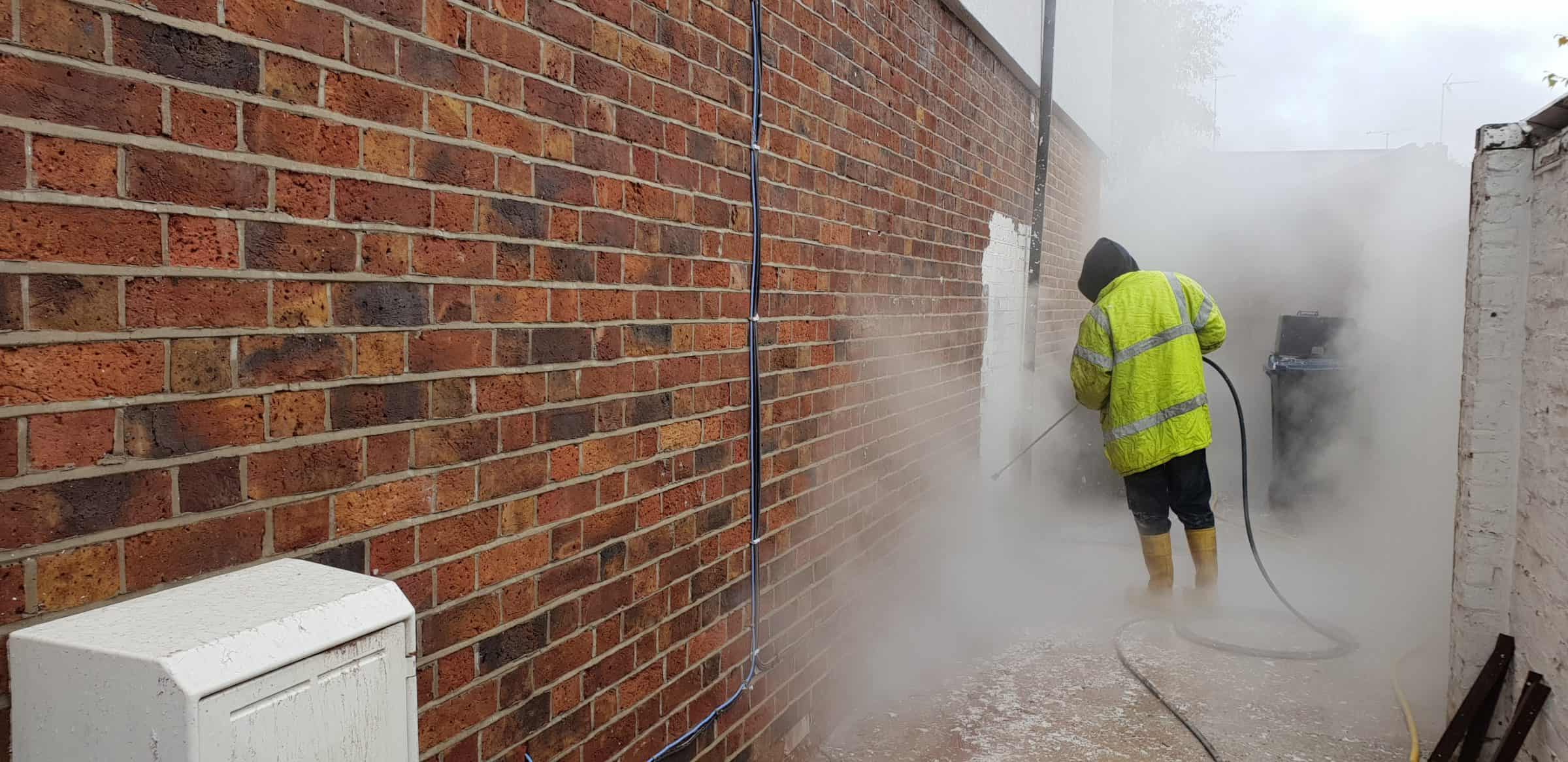 Steam cleaning paint off a brick wall, the cleaned brickwork showing against the painted section