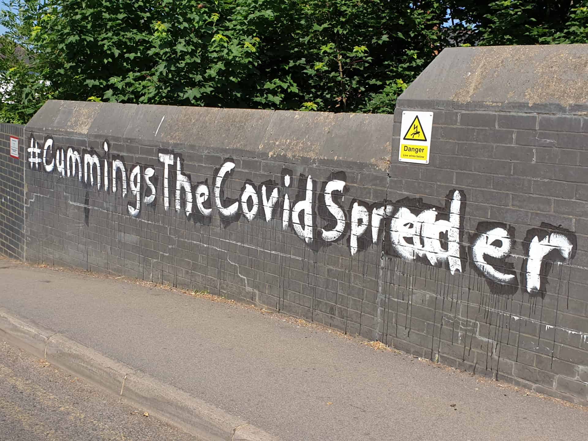 Large white painted graffiti slogan across a grey brick railway bridge parapet, before graffiti removal