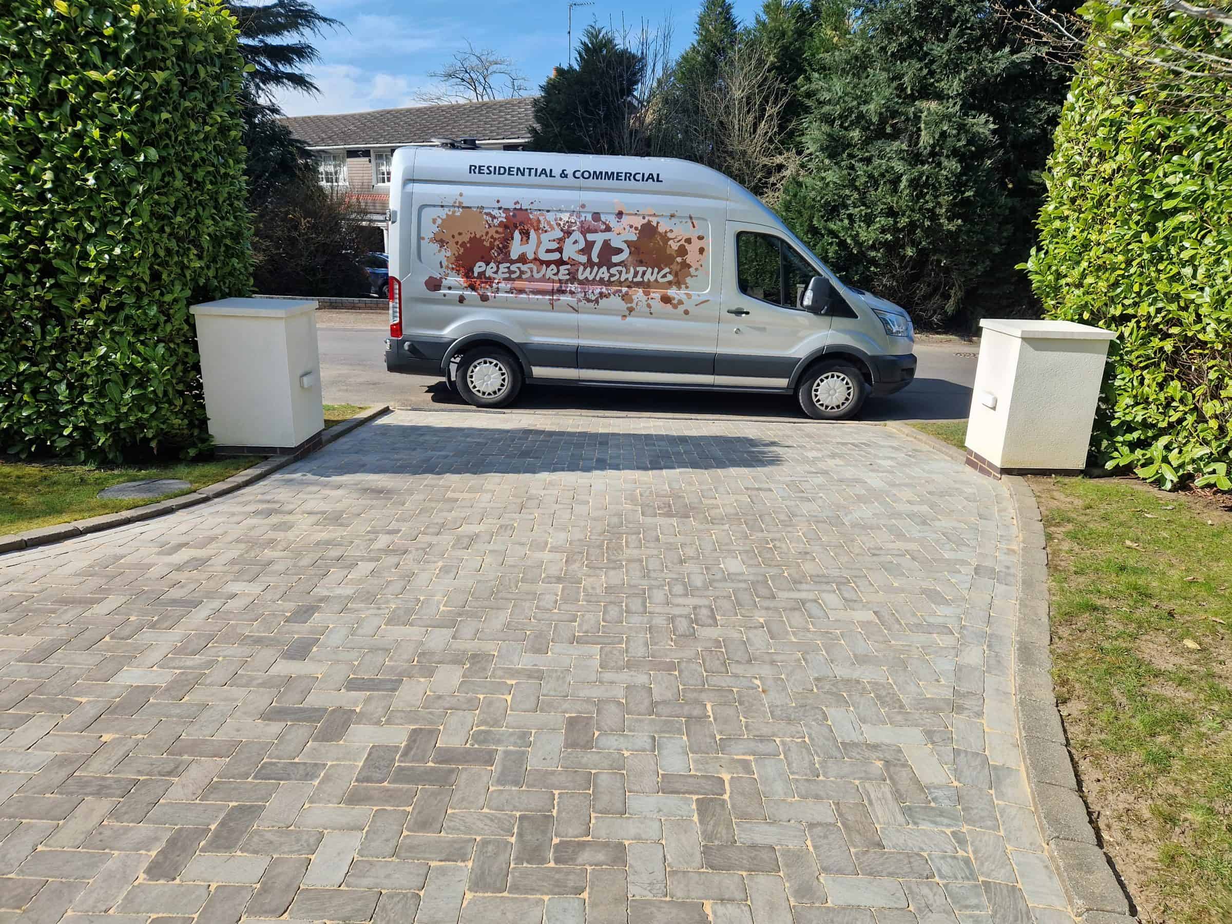 The Herts Pressure Washing van parked on a freshly cleaned block-paved driveway between clipped hedges