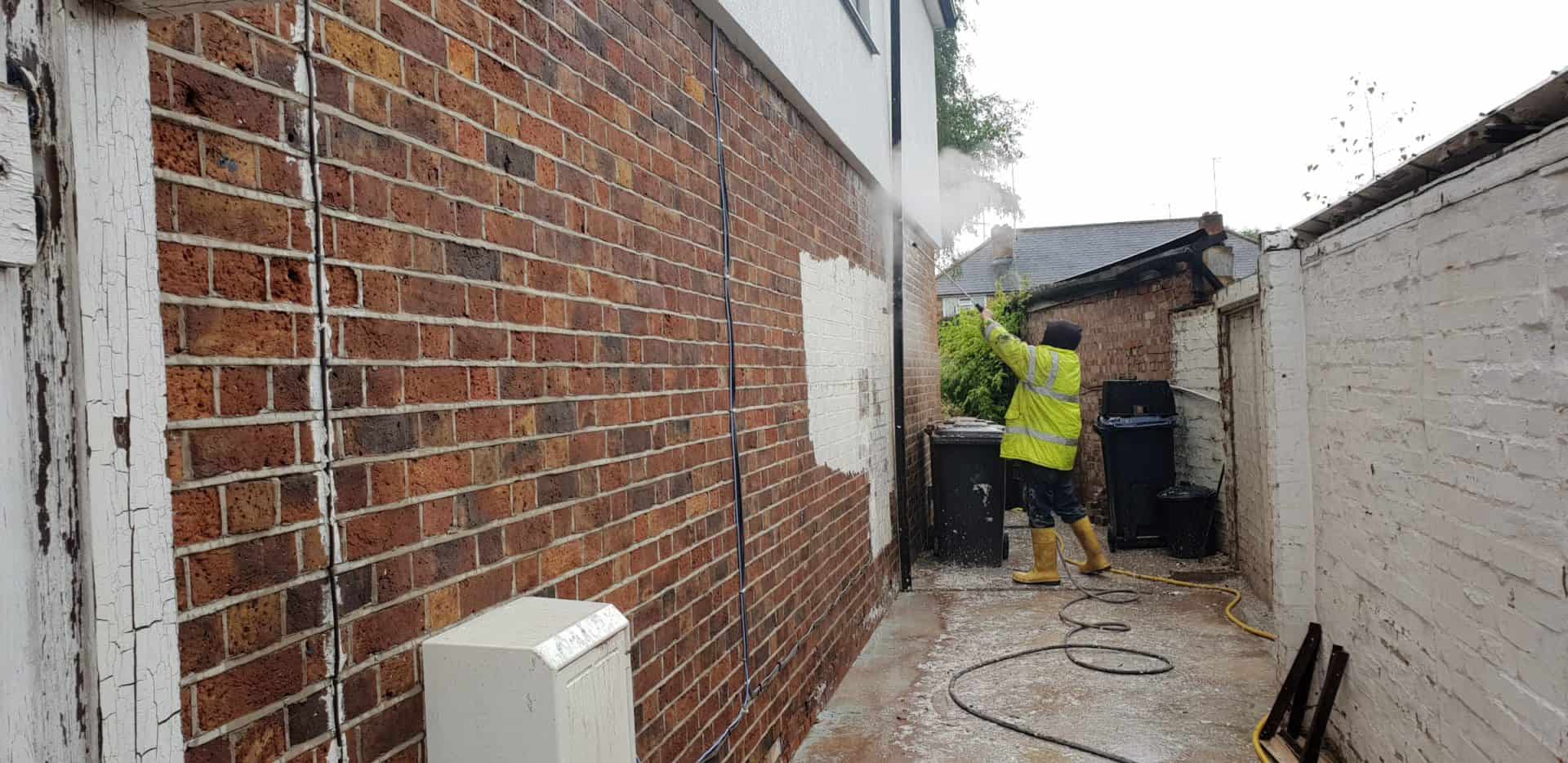 Paint being steam cleaned off a brick wall, the bare brick showing through where the paint has lifted