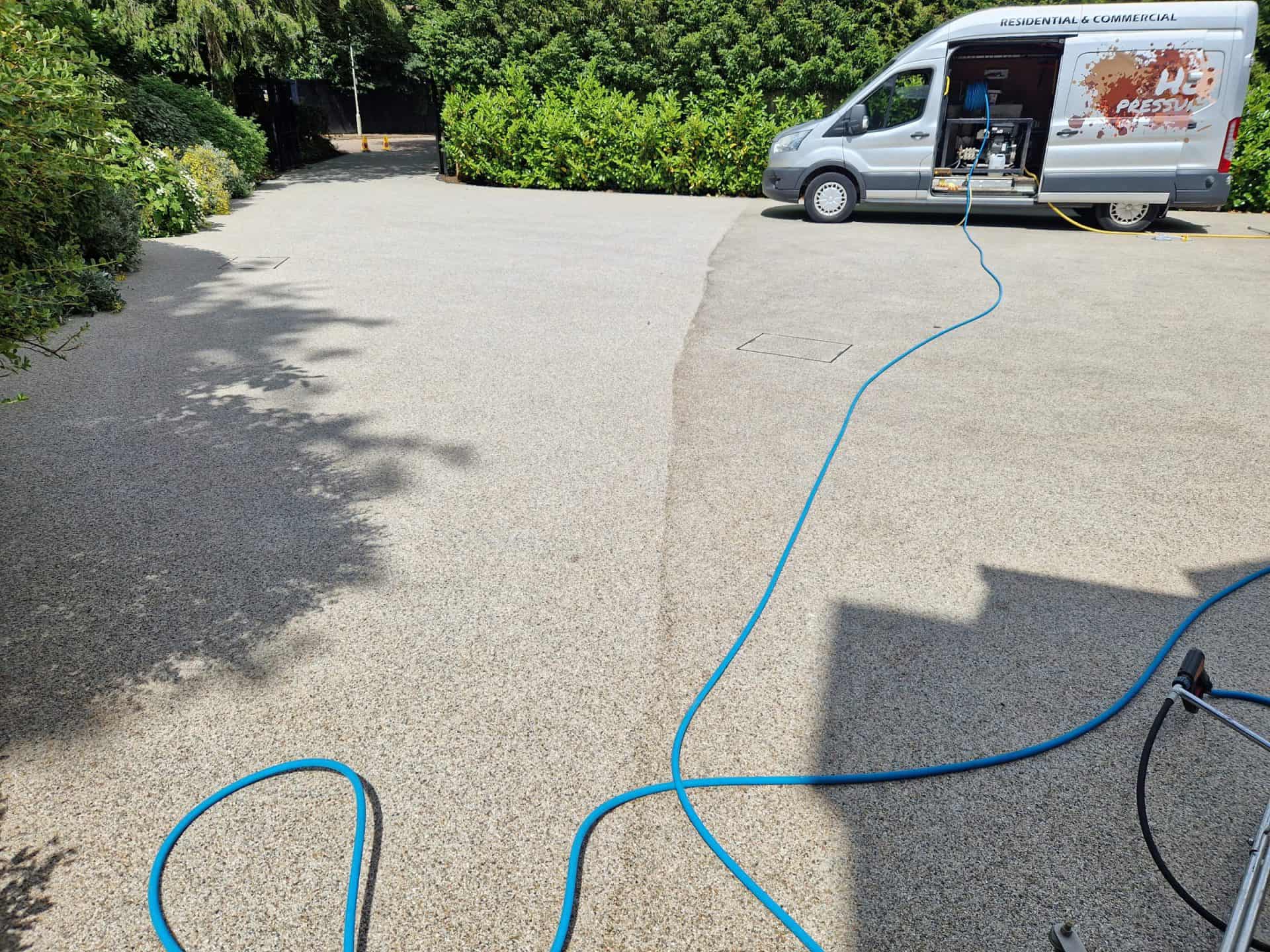 Commercial jetting van and hoses on a resin-bound driveway mid-clean, the cleaned half already lighter than the rest