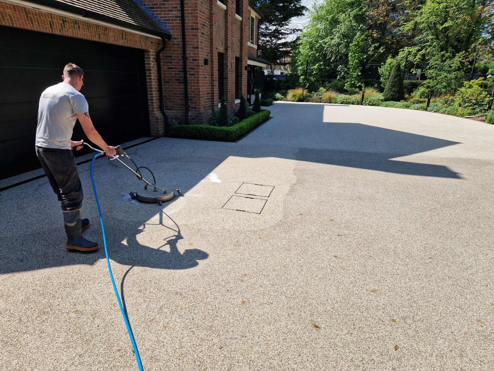 Rotary surface cleaner mid-pass across a resin-bound driveway, cleaned strip visible against the dirty section