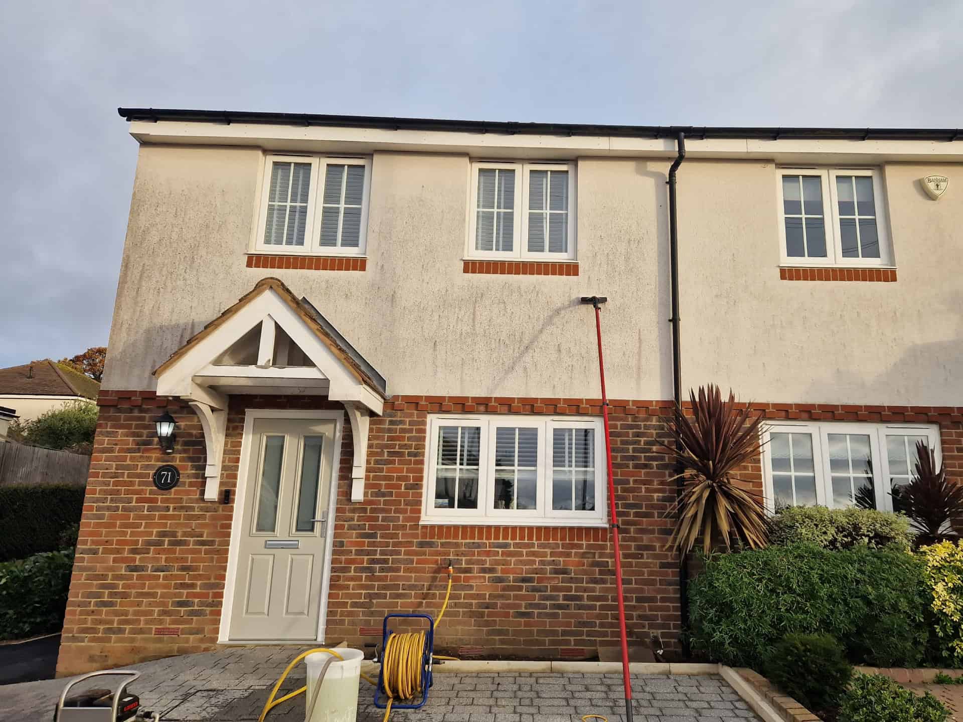 Mid-clean on a rendered semi-detached house – a water-fed pole is soft washing the upper render, with a clean strip already showing through the algae and black streaks
