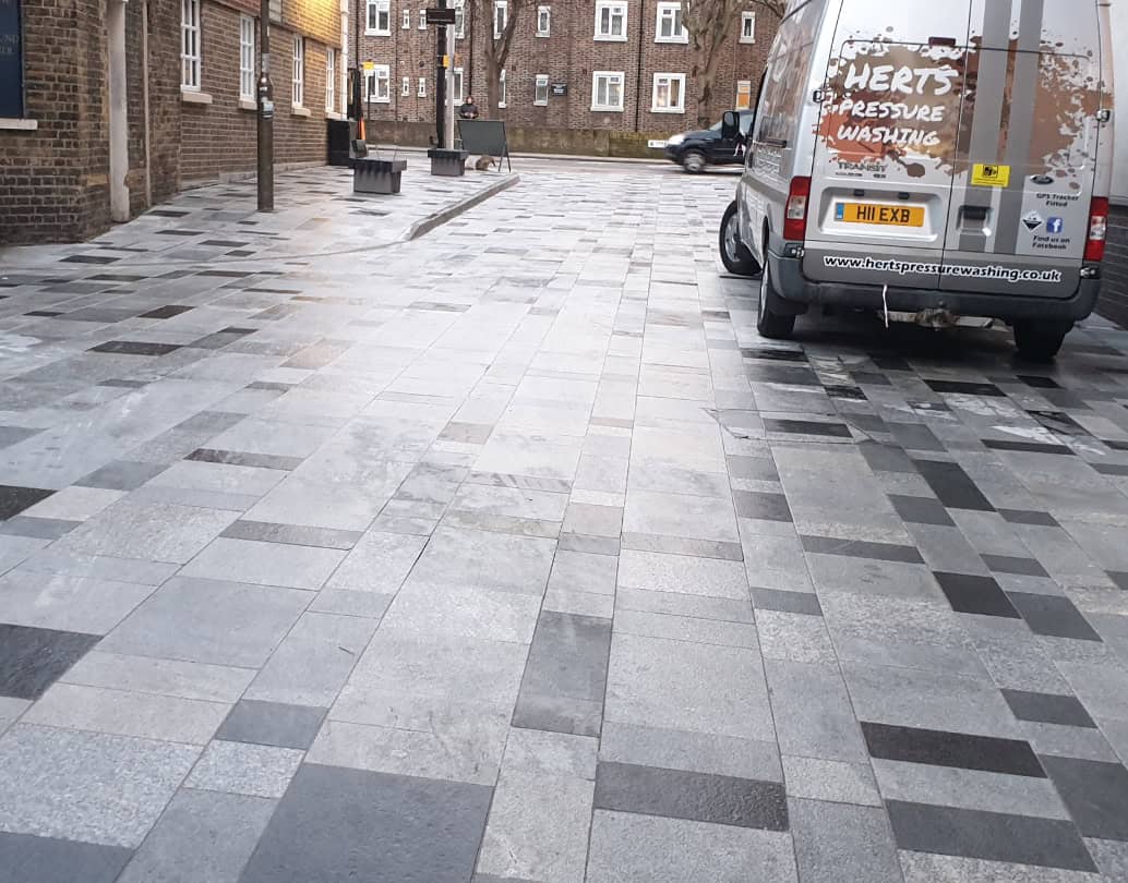 Granite paving in a pedestrianised street after pressure washing, with the Herts Pressure Washing van parked alongside