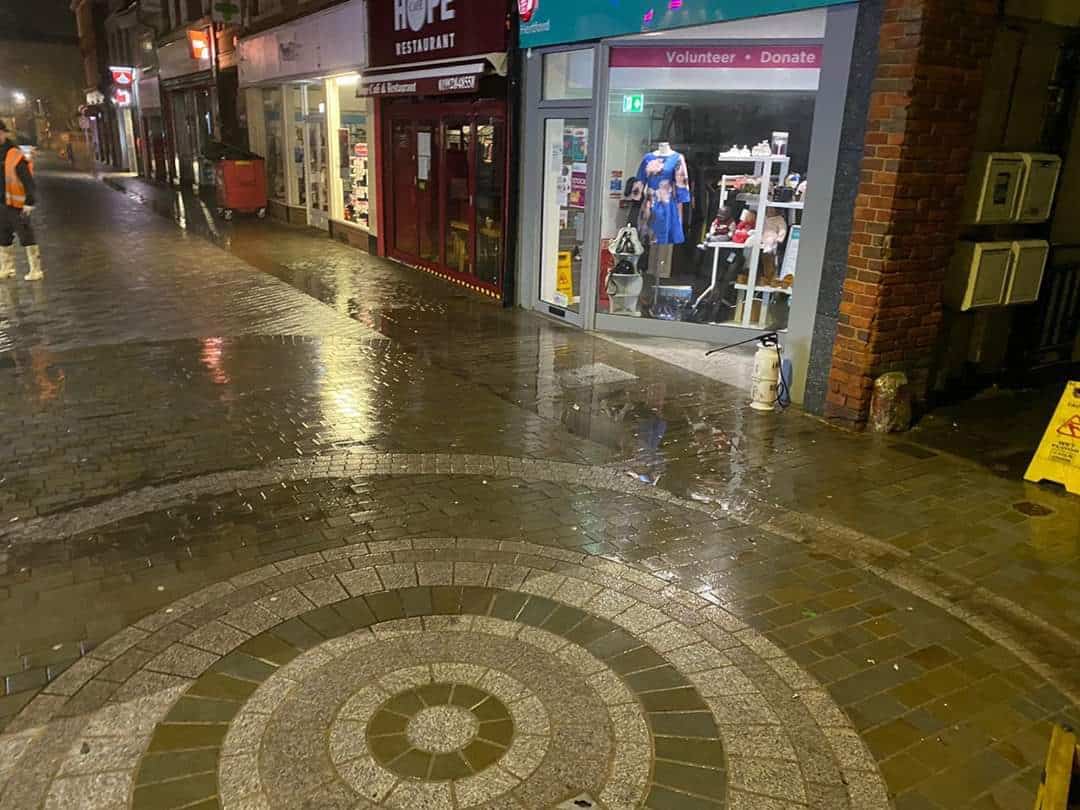 Freshly cleaned circular paving in Hertford town centre at night, wet after steam cleaning with shop fronts behind