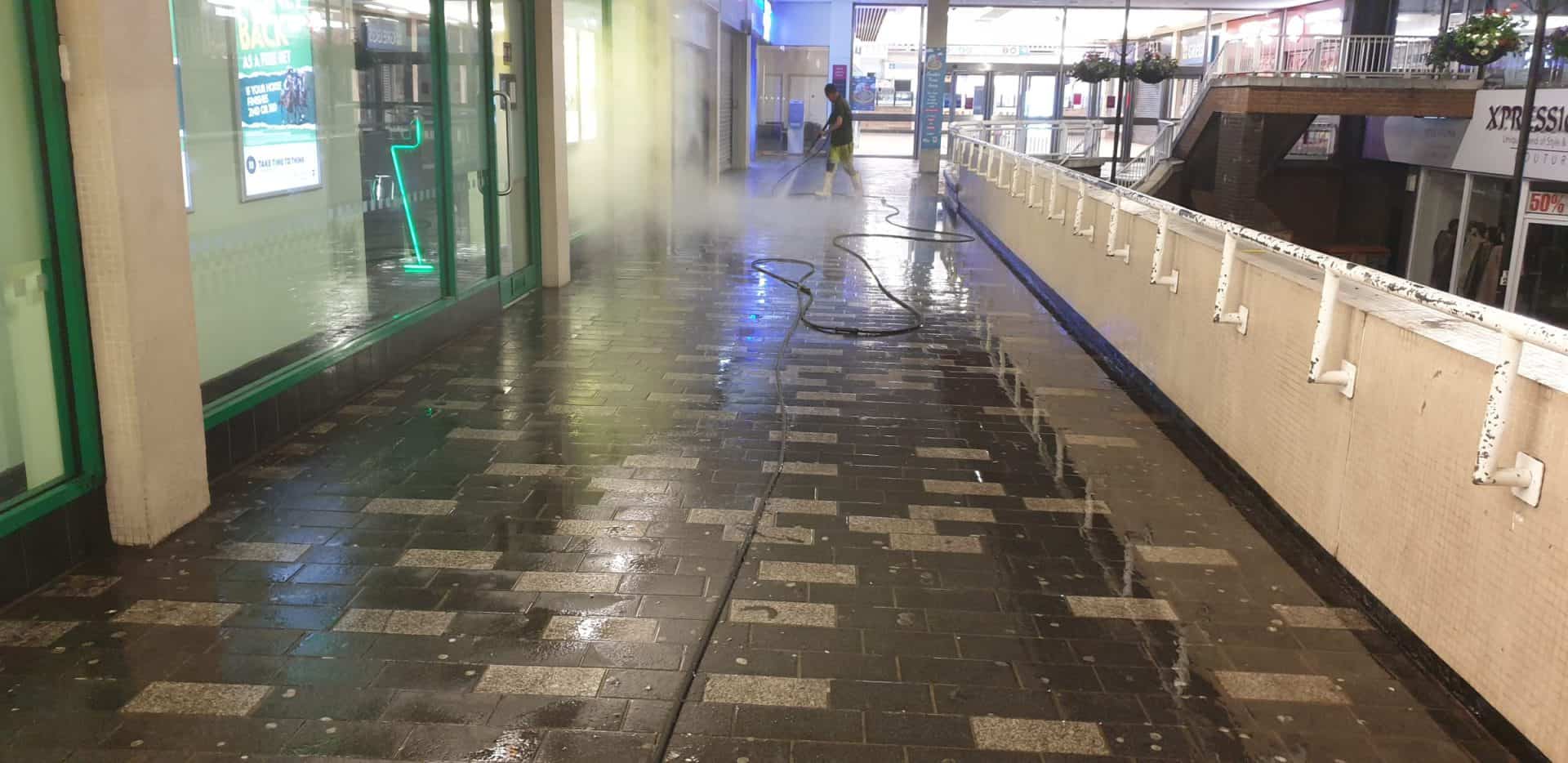 Steam cleaning paving in Luton town centre, steam rising ahead of the lance along a covered walkway