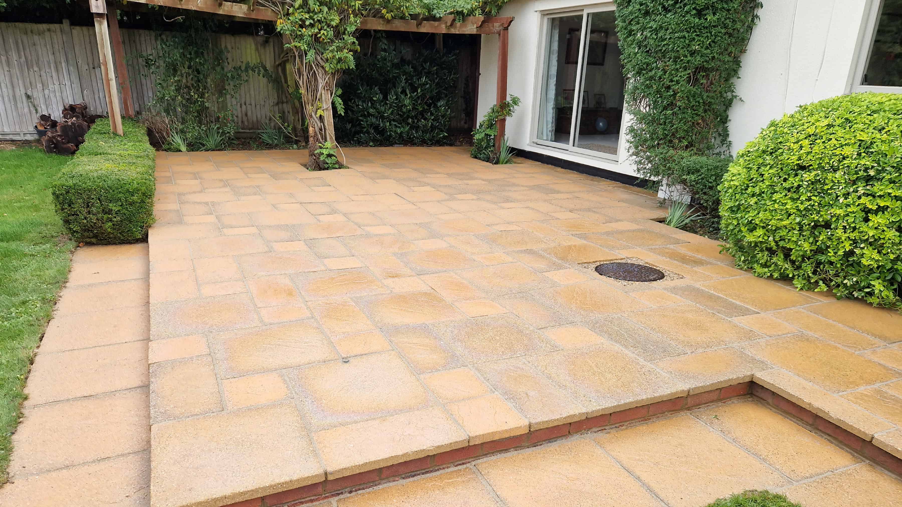 Clean buff patio after pressure washing, with a pergola and garden behind.